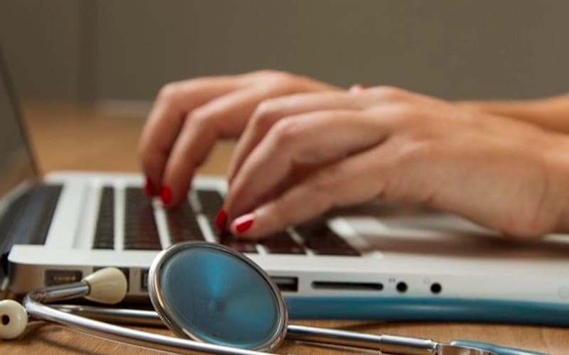 A clinician typing on a laptop beside a stethoscope
