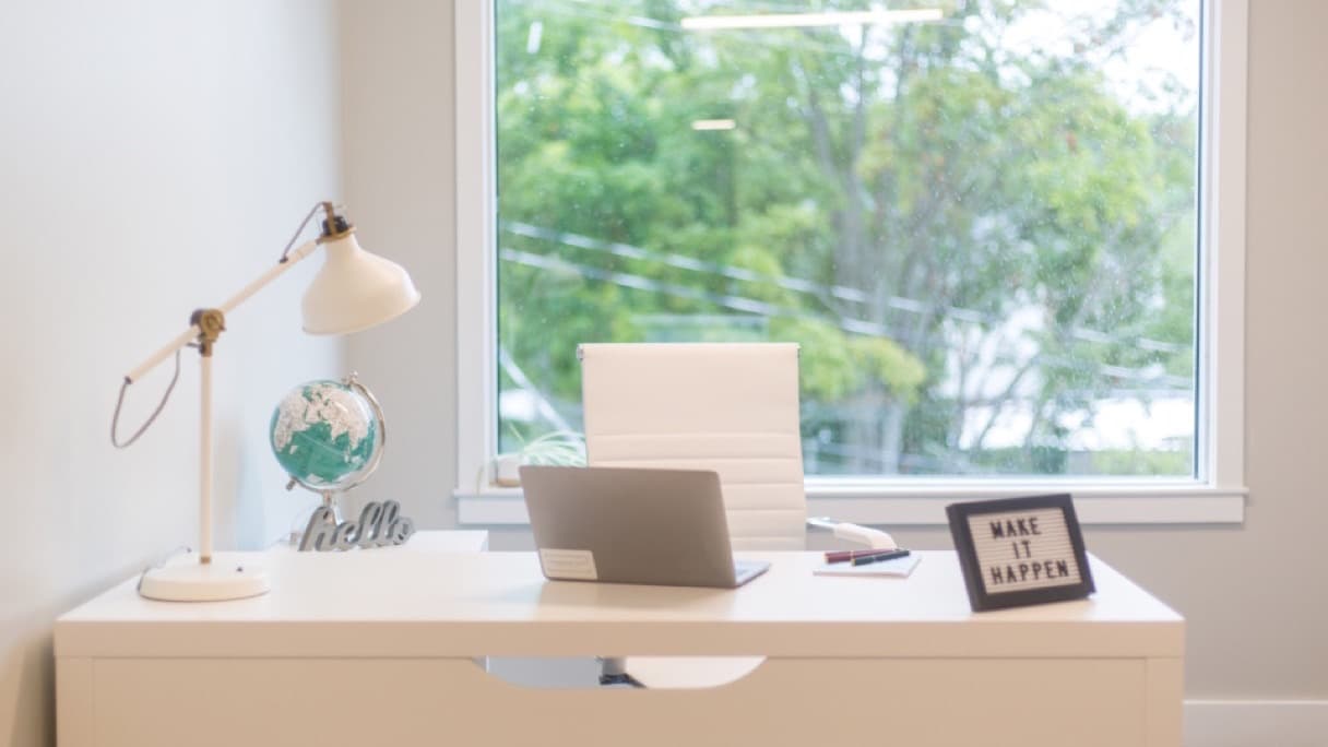 A laptop, notebook and mug on a home desk beside a window